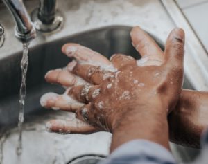 Two soapy hands rub together near a faucet with running water.